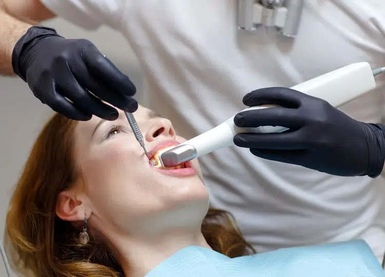 A woman laying on a dentist chair while a dentist is taking x-rays of her teeth with a special x-ray device