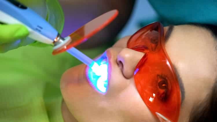 A woman wearing laser protection goggles as she opens her mouth to receive dental laser treatment