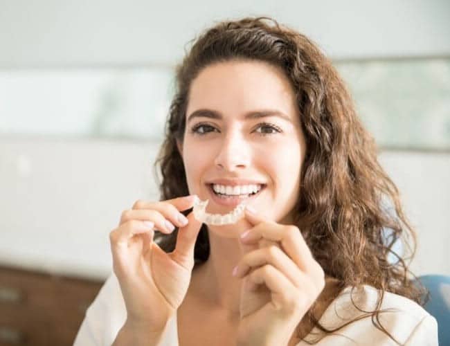 A woman holding an Invisalign set as she gets ready to put it in her mouth