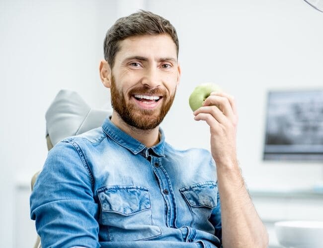 A man holding an apple in his left hand representing the strength of replacement dentistry treatments