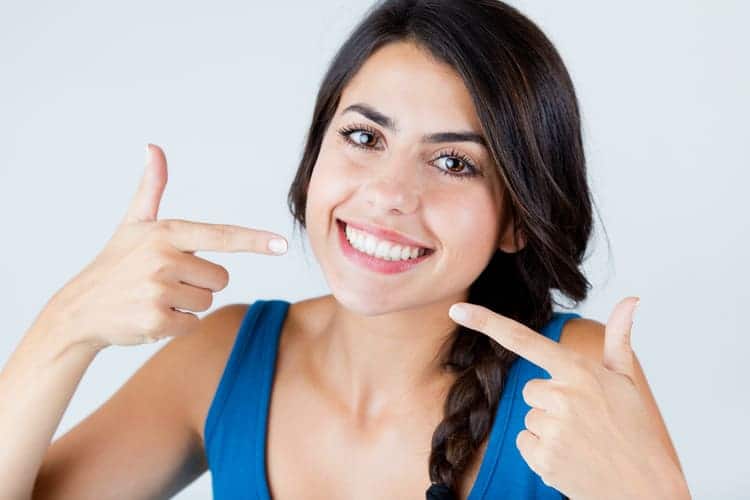 A woman smiling and pointing at her teeth after teeth whitening treatment